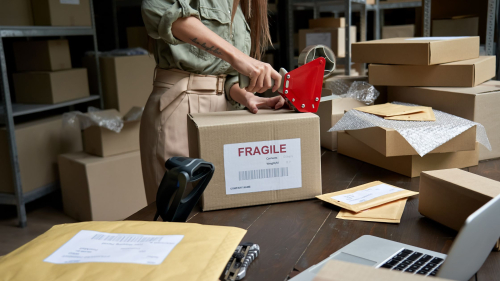 Female holding tape dispenser sealing a shipping box from an online store order